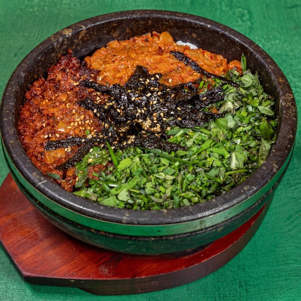 Korean bibimbap in a stone bowl with kimchi, seasoned seaweed, and fresh greens.