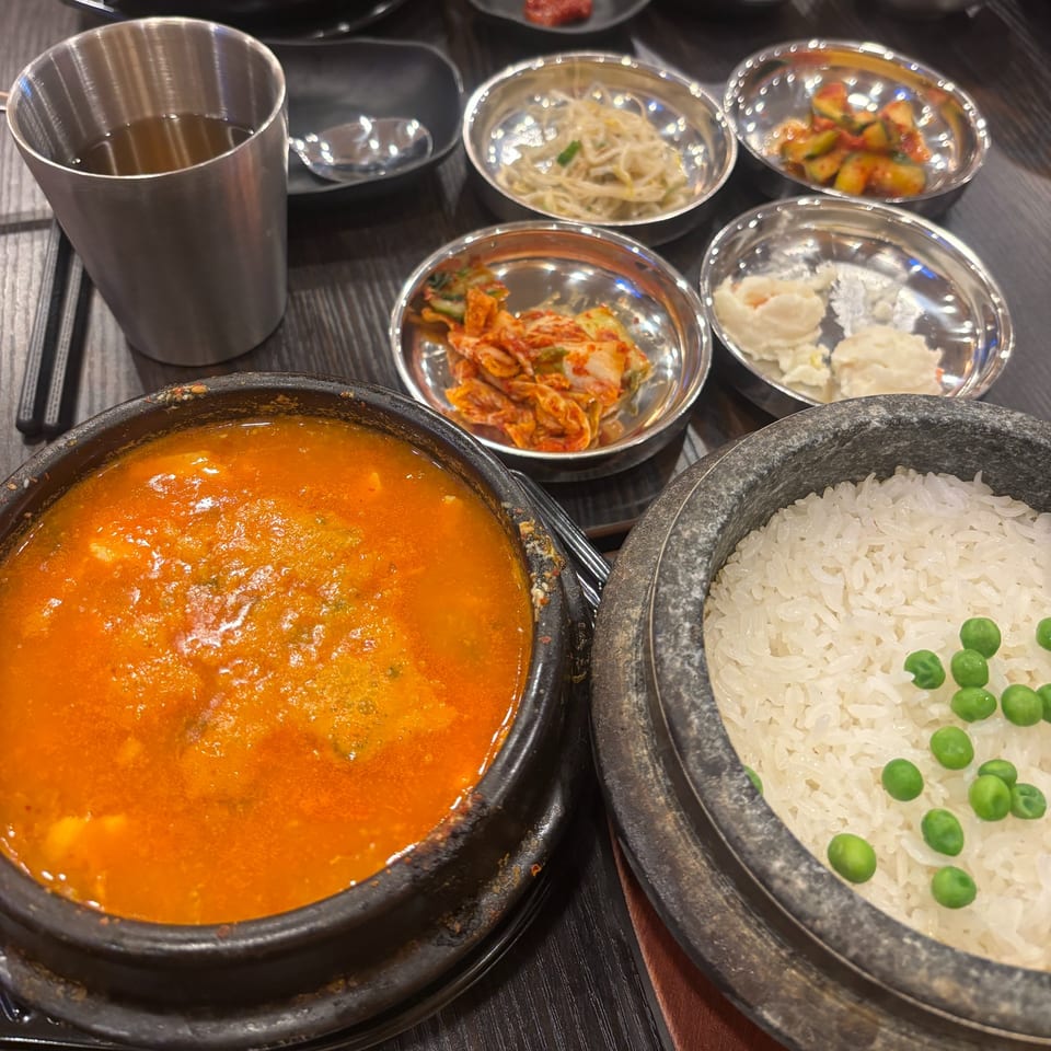 A Korean meal featuring a bubbling red stew, white rice with peas, and various banchan side dishes.