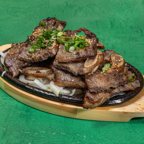 Korean BBQ short ribs (galbi) with sesame seeds and green onions on a sizzling platter.