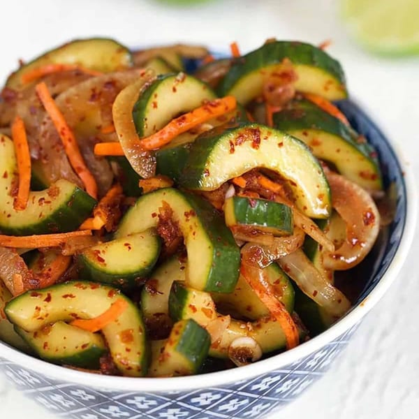 A close-up of Korean cucumber kimchi with carrots and onions in a blue and white bowl.