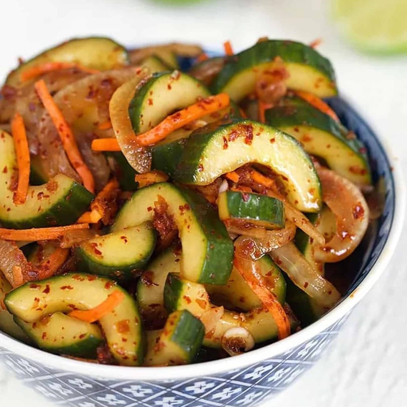 A close-up of Korean cucumber kimchi with carrots and onions in a blue and white bowl.