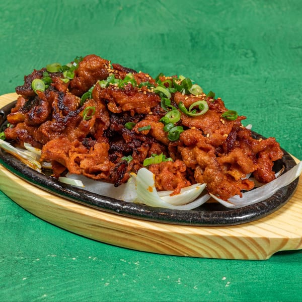 Spicy Korean pork bulgogi with green onions and sesame seeds on a sizzling platter.