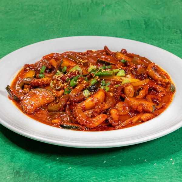 Spicy Korean stir-fried squid with vegetables, garnished with green onions and sesame seeds.