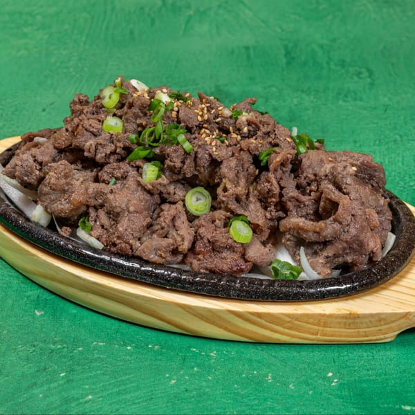 Korean bulgogi, thinly sliced marinated beef, garnished with green onions and sesame seeds on a hot plate.