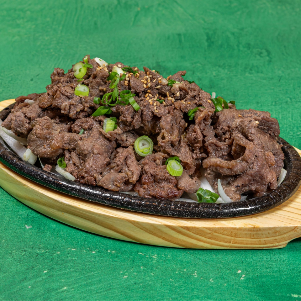 Korean bulgogi, thinly sliced marinated beef, garnished with green onions and sesame seeds on a hot plate.