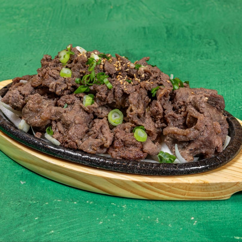 Korean bulgogi, thinly sliced marinated beef, garnished with green onions and sesame seeds on a hot plate.