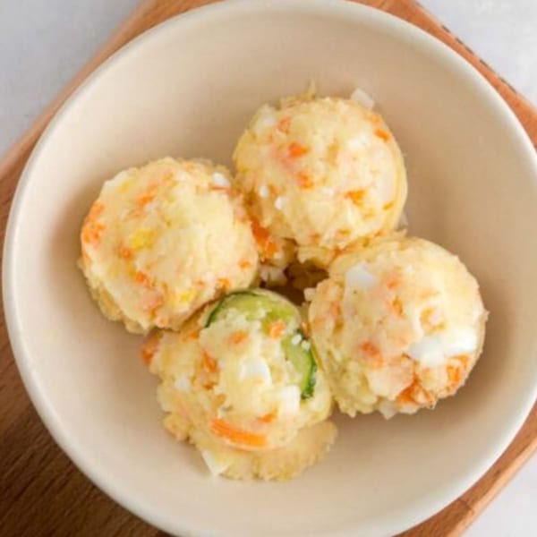 Four scoops of Korean potato salad with carrots, eggs, and cucumber in a light bowl.
