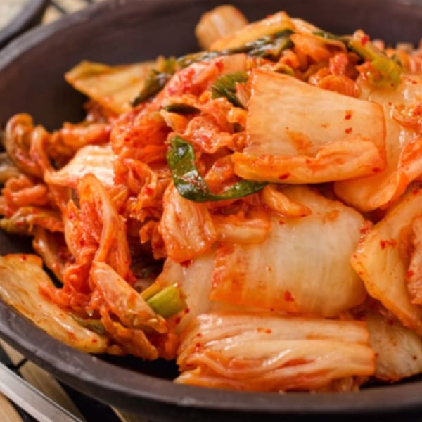 Close-up of vibrant red kimchi with green onions in a dark bowl, a Korean side dish.