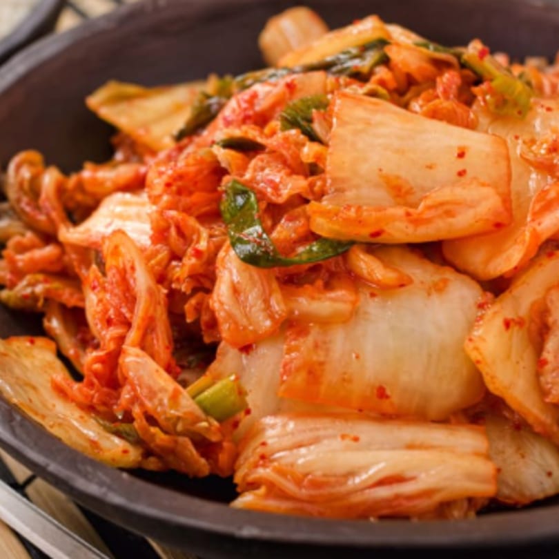 Close-up of vibrant red kimchi with green onions in a dark bowl, a Korean side dish.